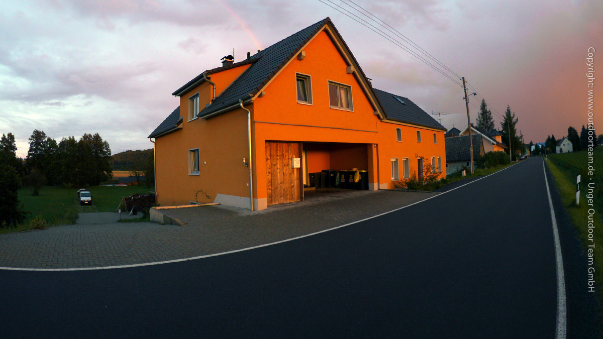 markant ist das orangefarbene Doppelhausgebäude der Herberge zu erkennen. Links (bergab) biegt man zum hauseigenen Parkgelände ab.