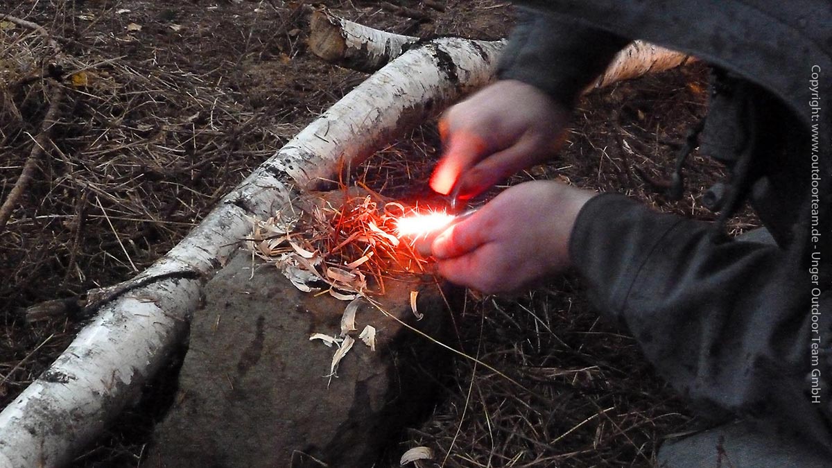 Funken schlagen mit einem einfachen Feuerstahl - als Grundlage Zundermaterial aus Birkenrinde, Distelsamen und trockenen Ästchen